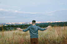 a man standing in a field of tall grasses praying over city