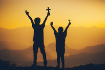 silhouettes of two people holding christian cross for worshipping God at sunset 