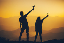 silhouettes of two people holding christian cross for worshipping God at sunset 