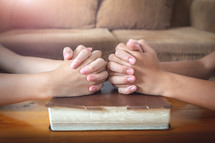 two people with praying hands over a Bible 