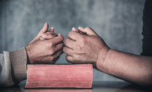 two people with praying hands over a Bible 