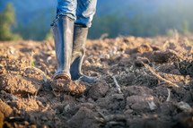 man with rubber boots tilling soil 