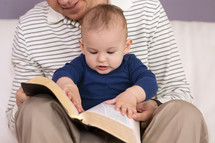 father and infant son reading a Bible together 