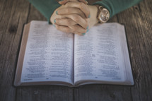 Hands folded in prayer on an open Bible