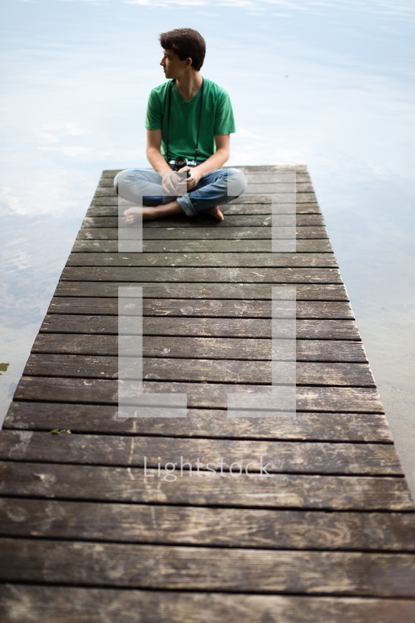 Man sitting at the end of a wooden pier on a lake.