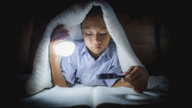 a boy reading a Bible under a blanket 