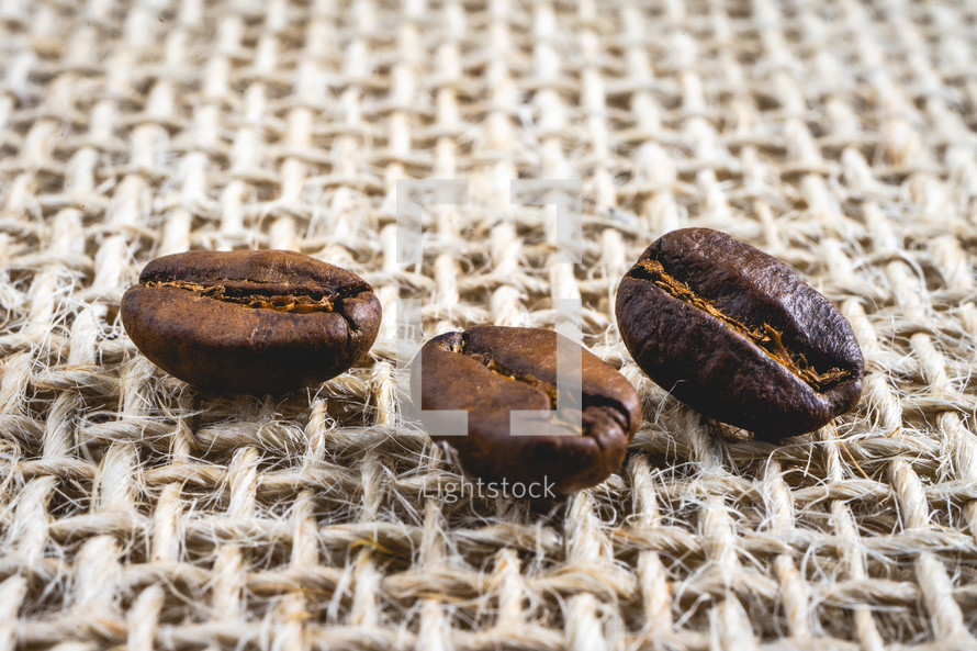 Close up from a few coffee beans laying down on a Burlap fabric background. Background voor coffee related products.
