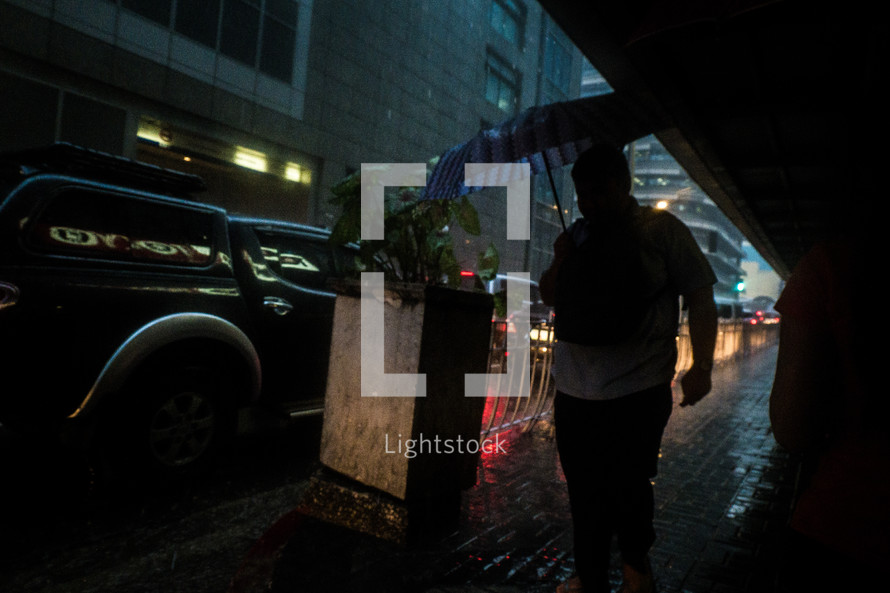 a man carrying an umbrella walking on a city sidewalk in the rain 