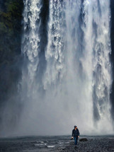 a man walking in front of a waterfall carrying a camera 