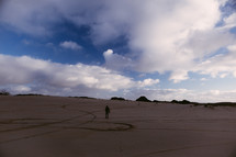 man walking up sand dunes 