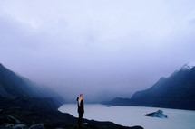 a woman standing by a mountain lake in fog 
