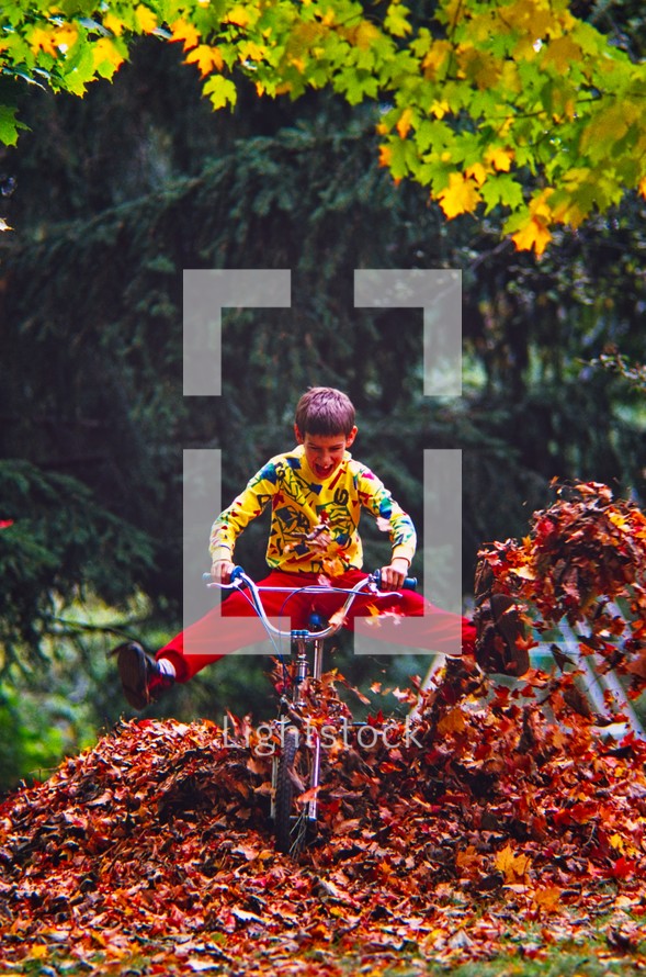 boy riding a bike through a pile of fall leaves 