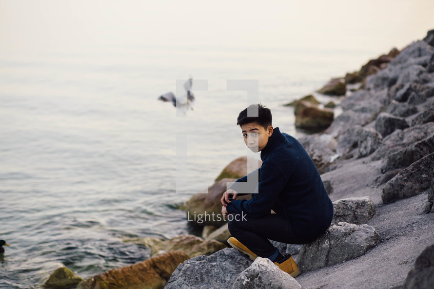 man sitting on rocks by the ocean 