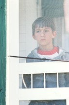 a boy child looking through a screen door 