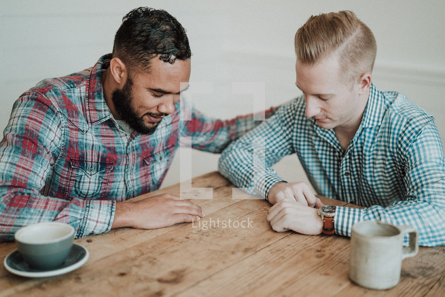 two men sitting at a table praying together 