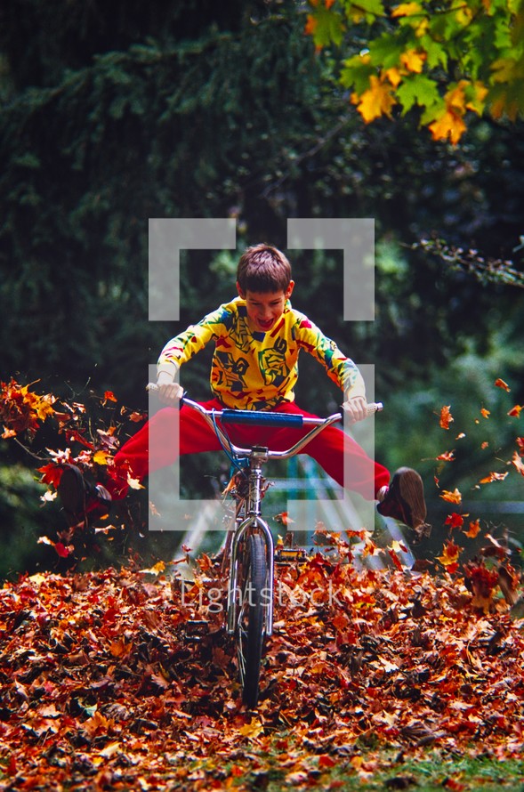 boy riding a bike through a fall pile of leaves 