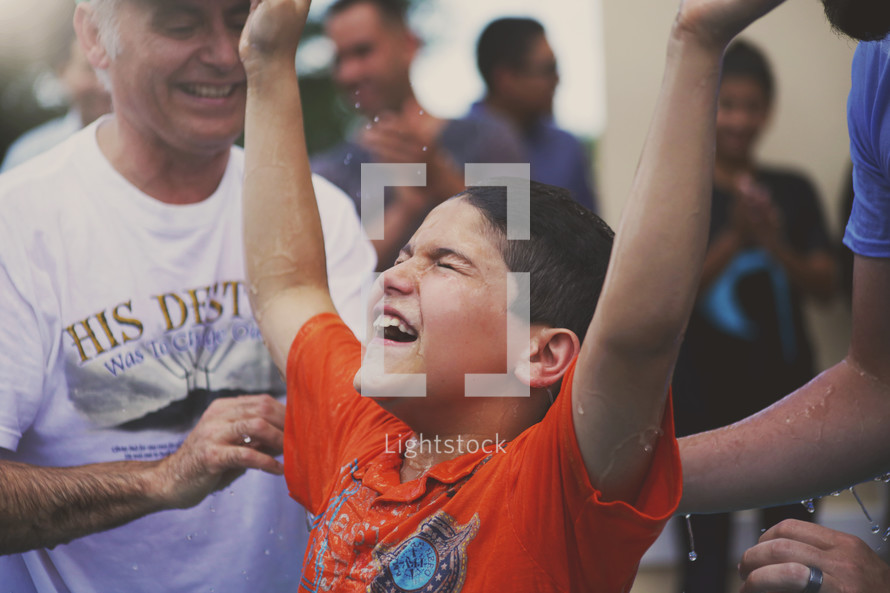 A little boy raises his arms after being baptized.