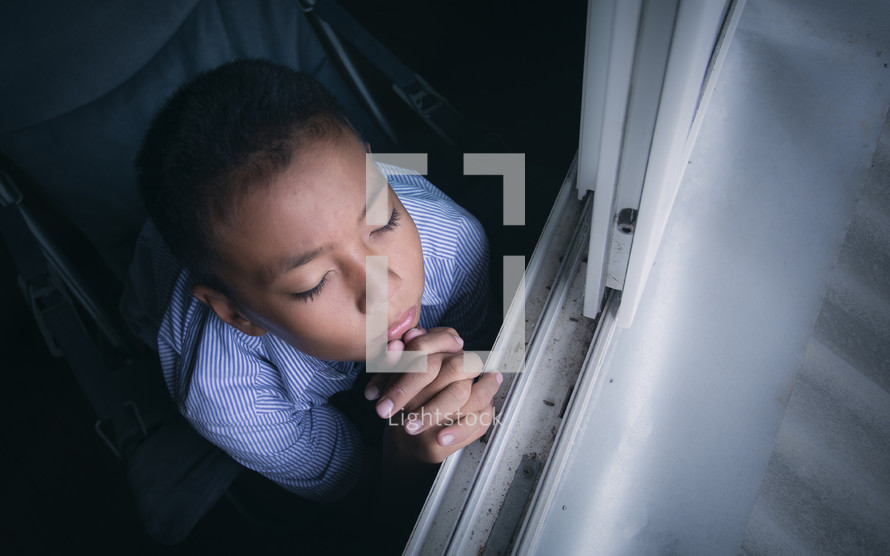 a boy praying beside of a window 