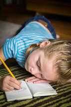 A girl writing in a notebook with a pencil.