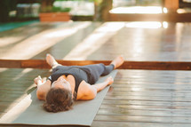 Unrecognizable young woman working outdoors, doing yoga exercise on grey mat, lying in Shavasana - Dead Body Posture, resting after practice, meditating, class. Tropical island Bali.