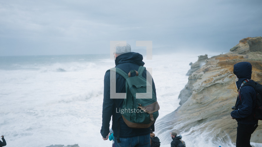 men with backpacks standing on a rocky coastline 