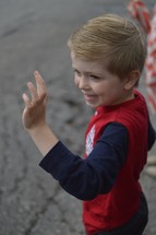 a boy child waving at a parade 