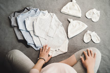 Pregnant unrecognizable woman sitting with baby clothes. Top view.