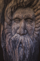 Man's bearded face carved into wood.