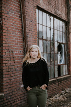 senior portrait of a young woman standing in front of a brick warehouse 