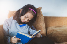 a girl reading a book sitting on a couch 