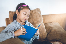 a girl reading a book sitting on a couch 
