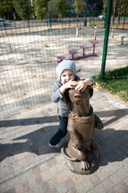 toddler hugging a dog statue 