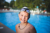 a boy child at a pool with goggles on his head 