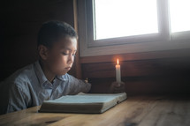 a boy reading a Bible by a window 