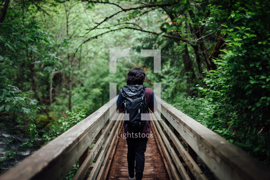 Man walking over a bridge with a bagpack.