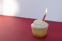 Vanilla cupcake with one candle on a red table and white background