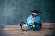 reading glasses and globe with graduation cap in a classroom 