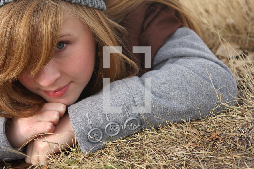 A young woman lays on the ground in dead grass.