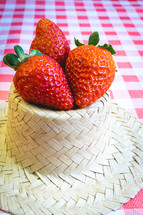 Fresh strawberries decorated on a straw hat. on a red picnic blanket.