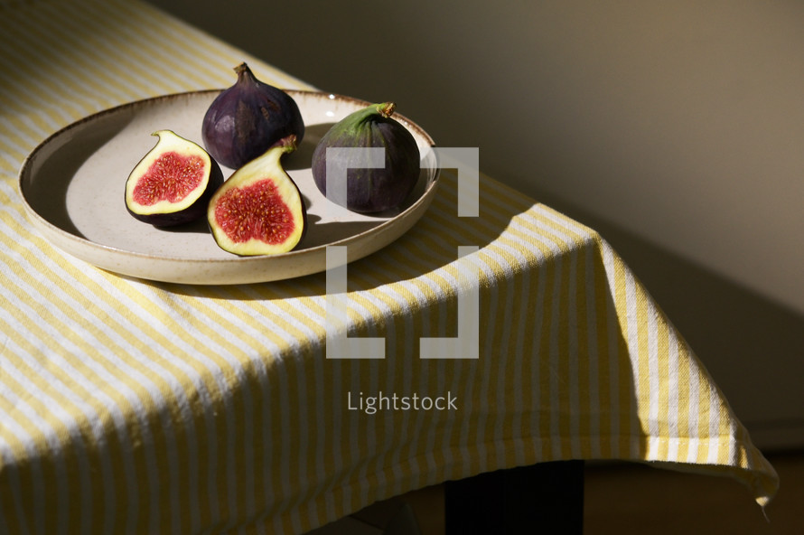 Figs fruits placed on a small plate on a table with a tablecloth and sunshine