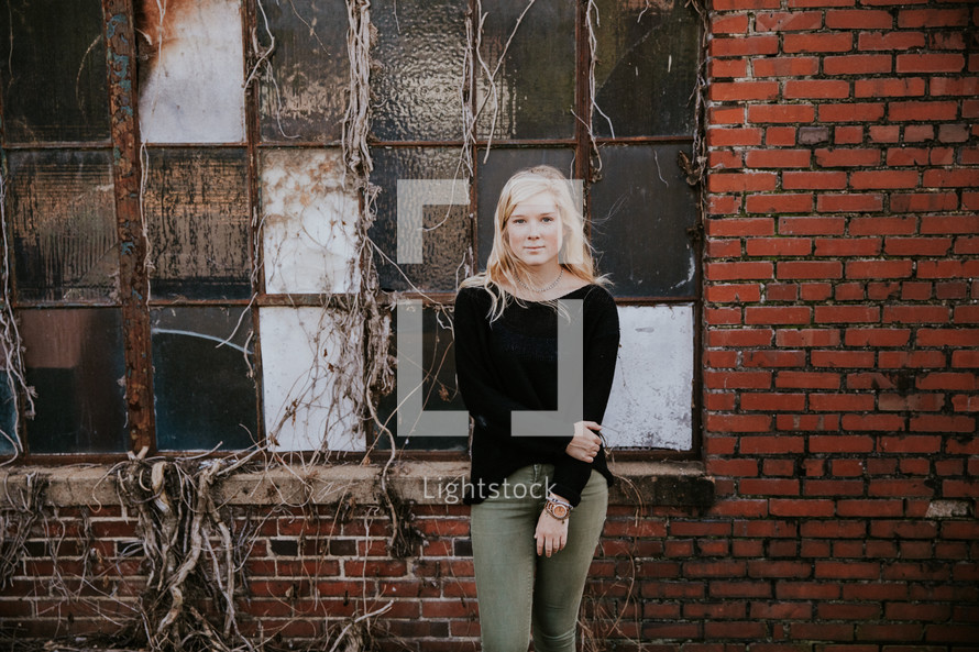 a young woman standing in front of a brick warehouse 
