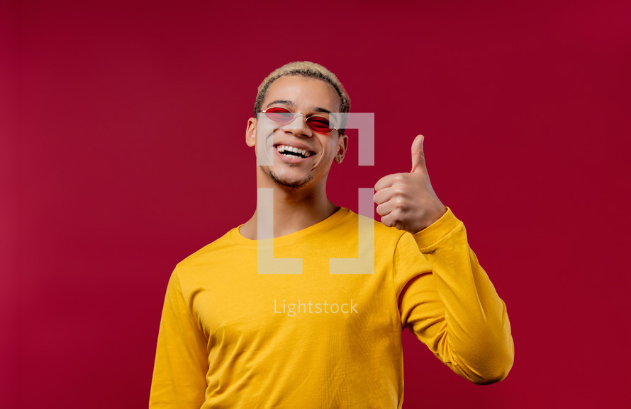 Positive curly man makes hand sign like, thumbs up gesture. Happy student guy in yellow, correct perfect choice, great deal, studio background. High quality