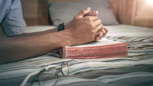 praying hands on a Bible kneeling at a bed 
