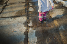 a child in snow boots standing on a sidewalk in winter 