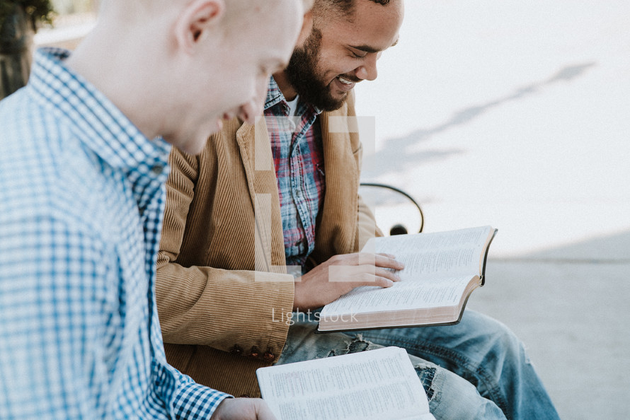 two men sitting on a park bench reading Bibles and discussing scripture 