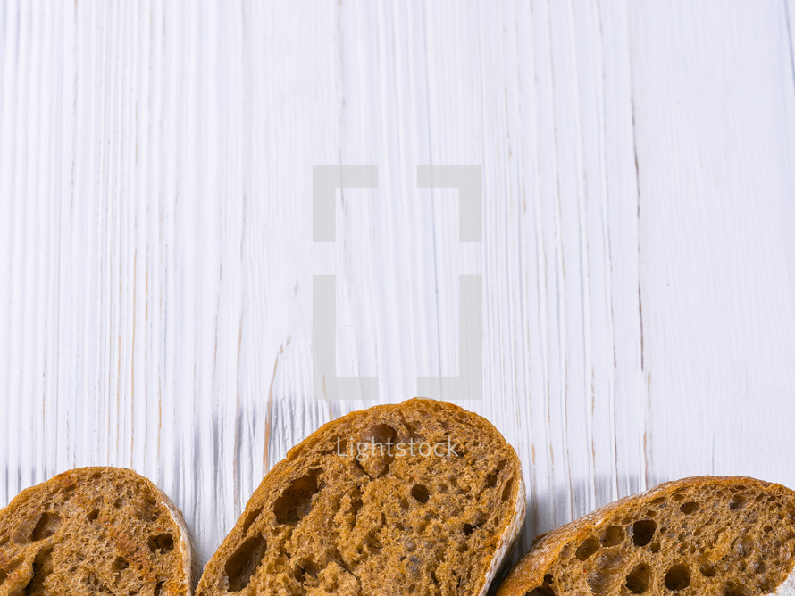 Wholemeal bread slices isolated on white wooden shabby table background. Frame photo. Copy space.