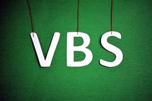 The letters, "VBS," hanging from strings on a green background.