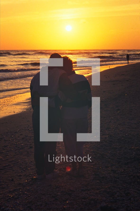 a couple snuggling on a beach at sunset 