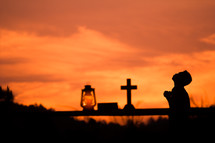 silhouette of a boy reading a bible and praying with Oil lamp on wood at sunset against an orange sky 