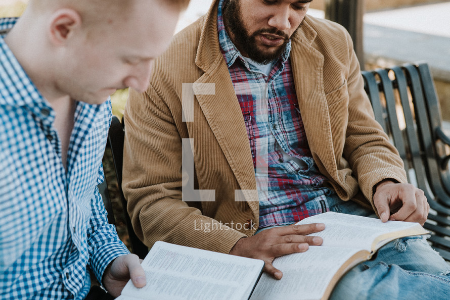 two men sitting on a park bench reading Bibles and discussing scripture 
